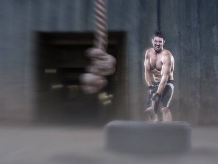 Athlete without shirt hitting a tire with a sledgehammer on the street