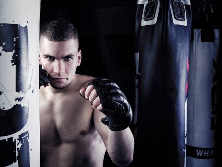 Muscular fighter in a fighting guard next to punching bag isolated on black background