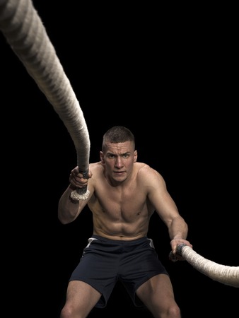 Athlete working out with battle ropes on black background