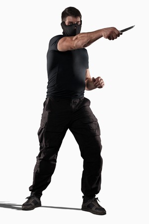Man in black uniform attacking with knife isolated on whiteの写真素材