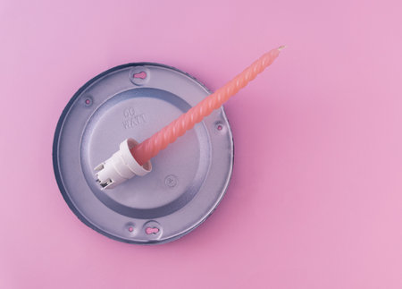One soft orange candle connected with the bulb spot on pastel pink background. Flat lay composition.の写真素材