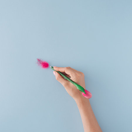 One small feather and the hand holding the pen on pastel blue background. Minimal flat lay.の写真素材