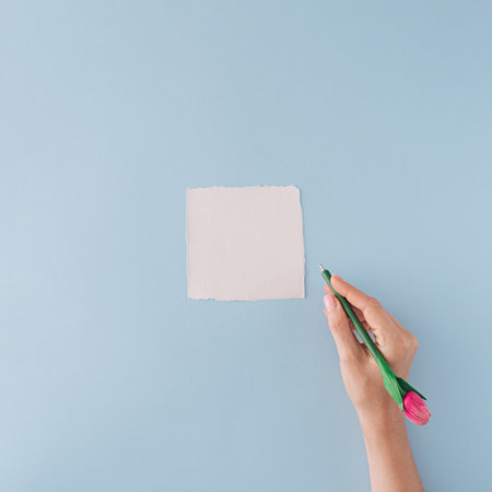 White paper card and the hand holding the pen on pastel blue background. Minimal flat lay.の写真素材