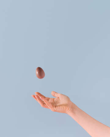 The girl's hand and one chocolate egg levitating in the air. Minimal Easter scene.の写真素材