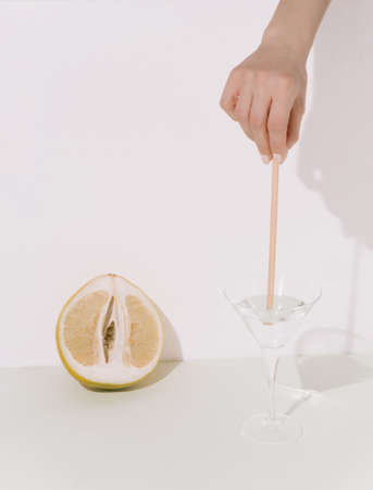 Pomelo, female hand, glass with liquid and bamboo stick on soft pastel background. Creative spring...