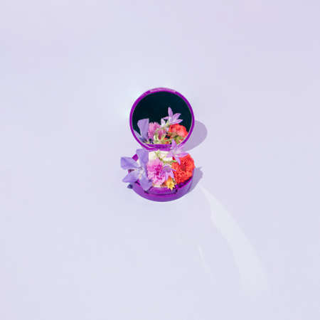 Face powder box with variant colorful spring or summer flowers. Pastel purple background. Minimal...