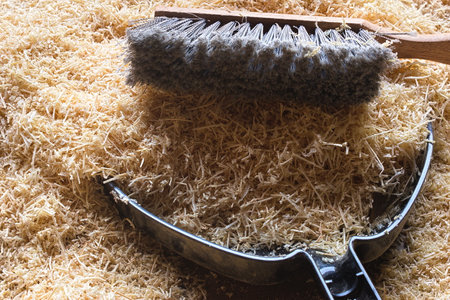 A woodworking dust pan and dust brush with the bristles facing towards the camera on a pile of wood shavings in a woodworking shop.の写真素材