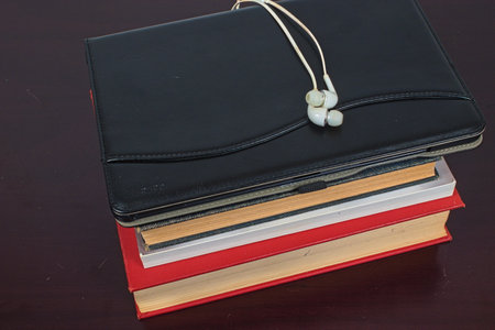 A pair of white earphones sitting on top of a closed tablet resting on top of a pile of books. Represents the the clash between traditional printの写真素材