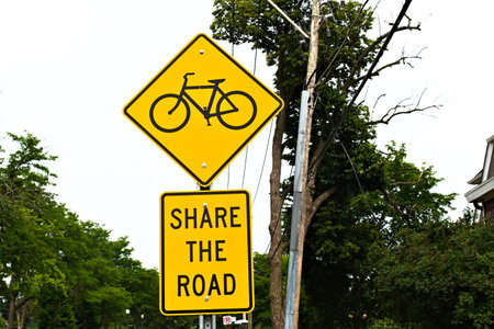 A share the road sign is posted along a road to encourage drivers to be aware that cyclists may be...