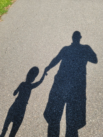 A photo of the shadow of a grandfather and grandson walking along the road.の写真素材