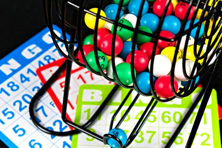 A colorful shot of a bingo cage, with multi-colored balls, sitting on a table with several bingo cards.の写真素材