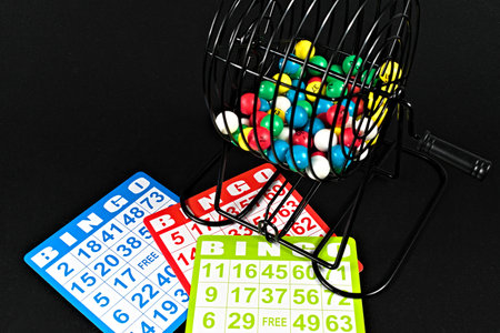 A wide shot of three bingo cards and a bingo cage with multi-colored balls sits on a black table.の写真素材