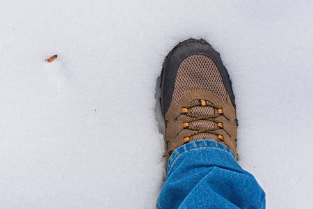 A first-person perspective shot of a brown and black hiking boot with orange laces sinking slightly...
