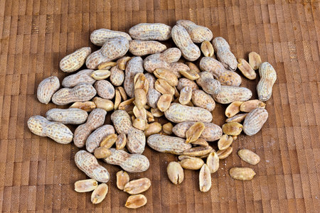 A scattered collection of whole peanuts and shelled kernels arranged on a woven bamboo mat,...