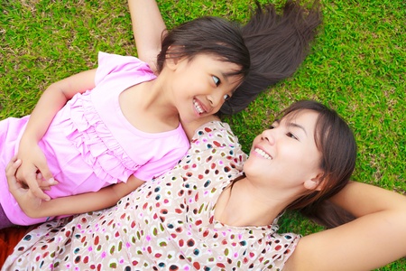 Mother and daughter laying on the green grassの写真素材