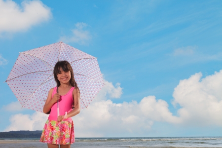 Smiling little girl at beach with pink umbrellaの写真素材