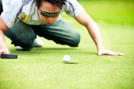 Golf player cheating blowing to get the ball into the holeの写真素材