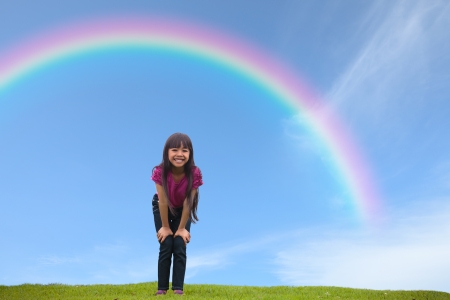 Smiling asian little girl standing on green grass under the rainbow, Outdoor Portraitの写真素材