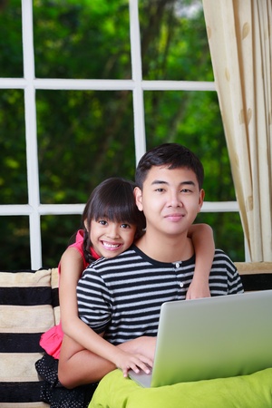 Little asian girl pointing on laptop with big brother at homeの写真素材