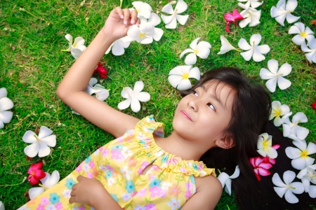 Little asian girl laying in green grass with frangipani flower in her handの写真素材