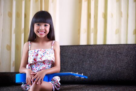 Smiling little asian girl sitting with ukuleleの写真素材