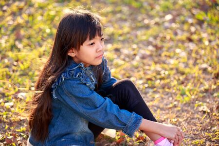 Beautiful little girl in jean coat looks on autumn parkの写真素材
