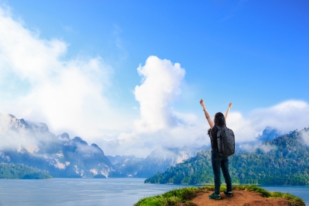 Young happy girl with backpack standing near big river with raised handsの写真素材