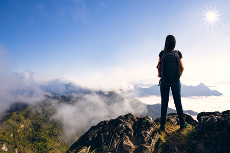 Young woman with backpack standing on cliffの写真素材