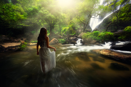 Young asian woman standing by a stream in the forestの写真素材