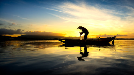 Silhouette asian fisherman on the boat in the morningの写真素材