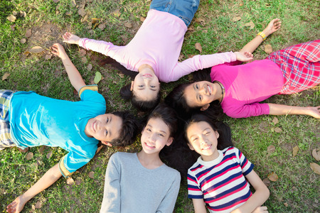 Smiling young boys and girls lying on green grass
