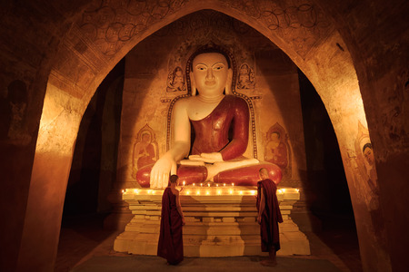Little monk praying with candles in front of buddha statue inside old pagoda, Bagan Myanmarの写真素材