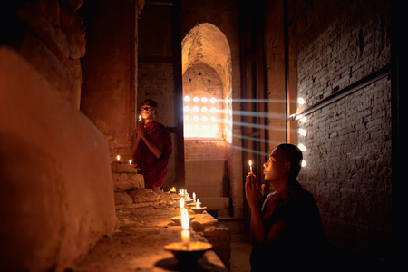 Novices praying with candles in front of buddha statue inside old pagoda, Bagan Myanmarの写真素材
