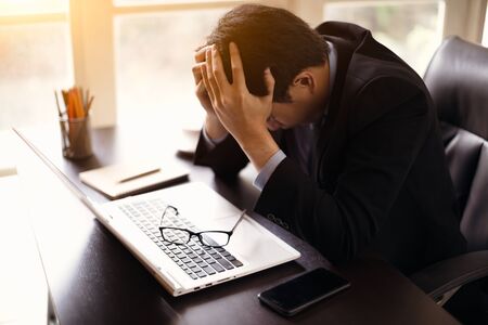 Stressed businessman sitting at workplace and touching his head