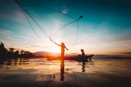 Silhouette of fishermen using nets to catch fish at the lake in the morningの写真素材