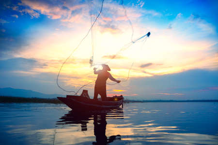Silhouette fisherman throwing fishing net during sunriseの写真素材
