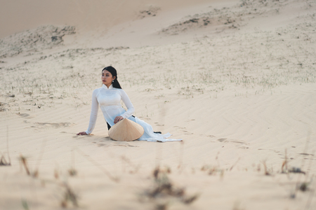 Beautiful vietnamese lady with vietnam culture traditional dress sitting at a white sand Mui ne, Ho Chi Minh City Vietnamの写真素材