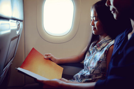 Mother with daughter sit on their place in airplane economy class and read a magazineの写真素材