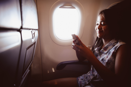 Adorable little girl traveling by an airplane child sitting by aircraft window and listen musicの写真素材