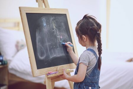 Litte girl draws a chalk on a blackboardの写真素材