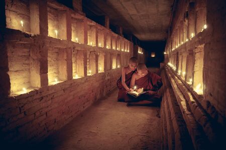 Young Buddhist novices are reading a book with light from candleの写真素材