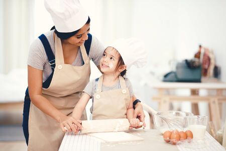Mother and daughter using a rolling pin together in the kitchenの写真素材