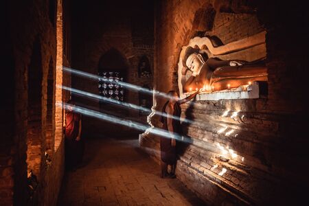 Novices praying with candles in front of buddha statue inside old pagoda, Bagan Myanmarの写真素材