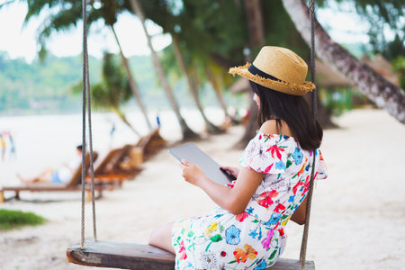 Young girl sitting on swing on the beach using digital tablet, Ko Kut Thailandの写真素材