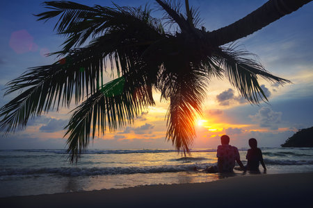 Rear view of teenage couple sitting on the beach at sunset, Koh Kut Thailandの写真素材