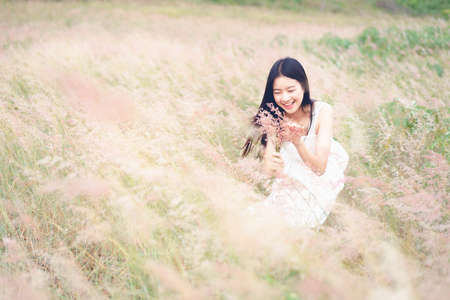 Asian woman in a white dress stands in the middle of pink field on a sunny dayの写真素材