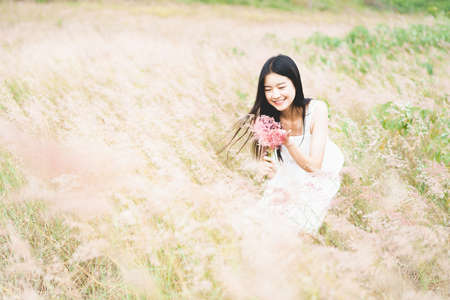 Asian woman in a white dress stands in the middle of pink field on a sunny dayの写真素材