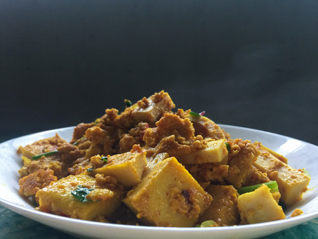 yellow curry tofu fried on white dish with hot smoke on black background.の写真素材
