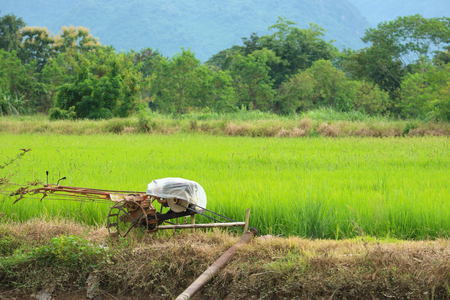 plowing machine on green rice field surrounded by natural tree and mountain.の写真素材