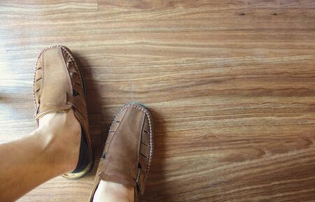 Man foot wearing casual leather shoes with wood floor background.
